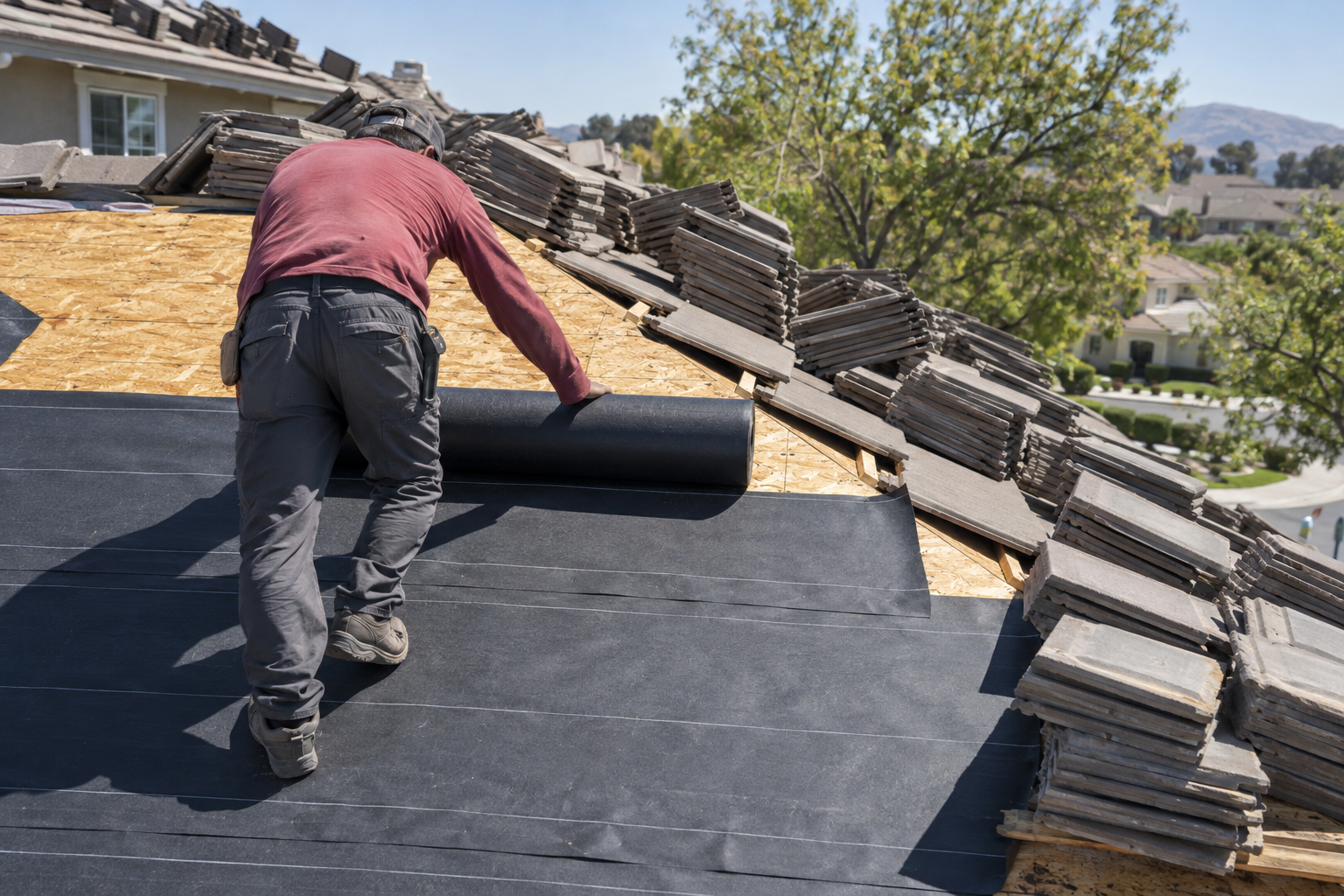 Concrete roof tiles stacked on a roof while new underlayment is rolled out beneath them