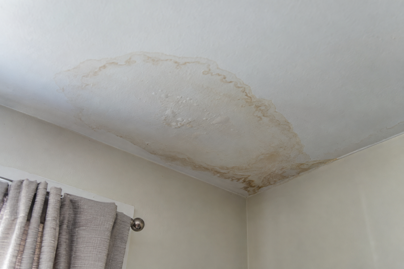 Brown water stain spreading across a bedroom ceiling into the corner